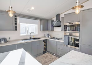Une cuisine moderne avec des meubles gris, une cuisinière à gaz, un four et deux lampes suspendues.