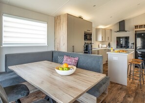 A modern kitchen with a central island, a dining area with a wooden table, and a seating area with a grey sofa. - 3 bedroom accommodation in Fowey (Fowey)