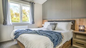 Un dormitorio con una cama, una mesita de noche con lámpara, una ventana con cortinas y un radiador.