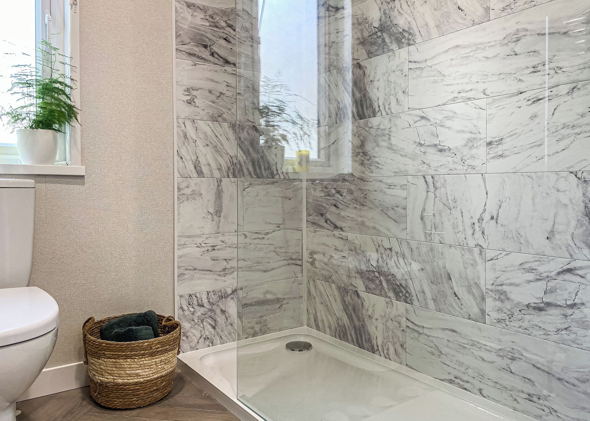 A bathroom with a toilet, a shower with marble tiles, and a wicker basket on the floor.
