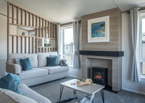 A modern living room with a sofa, a fireplace, a table, and a window with curtains. - 1 bedroom accommodation in Fowey (Fowey)