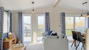 En stue med en sofa, et sofabord og et spiseområde med stole. Gardiner, en loftslampe og udsigt gennem glasdørene.