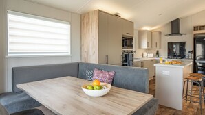 Ett modernt kök med en central köksö, inbyggda vitvaror och en sittgrupp med bord och kuddar.