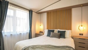 Une chambre à coucher bien aménagée, avec un grand lit, des tables de chevet, une tête de lit en bois et une fenêtre avec des rideaux.