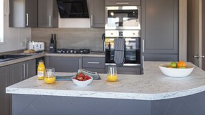 Une cuisine moderne avec des meubles gris, un îlot central agrémenté de corbeilles de fruits, un four à micro-ondes et une cuisinière.