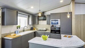 Une cuisine moderne avec des meubles gris, un îlot en marbre, un four encastré et des luminaires suspendus.