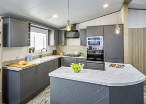 Une cuisine moderne avec des meubles gris, un îlot en marbre, un four encastré et des luminaires suspendus.