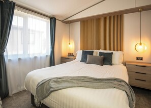 Un dormitorio ordenado con una cama grande, mesitas de noche y una lámpara fijada a la pared.