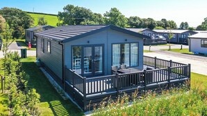 A mobile home with a balcony, a small porch, and a grassy yard. - Exclusive 3 Bed (Pet) (Fowey)