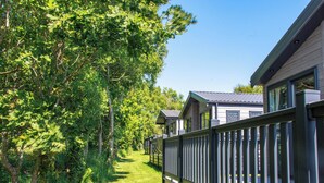 A row of modern cabins with a wooden fence, surrounded by lush greenery and trees. - Exclusive 3 Bed (Pet) (Fowey)