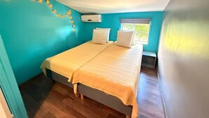 Un dormitorio con cama, almohadas, una ventana y un aire acondicionado de pared.