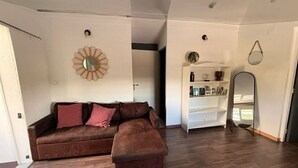 Una sala de estar con un sofá seccional marrón, una estantería blanca y un espejo redondo.