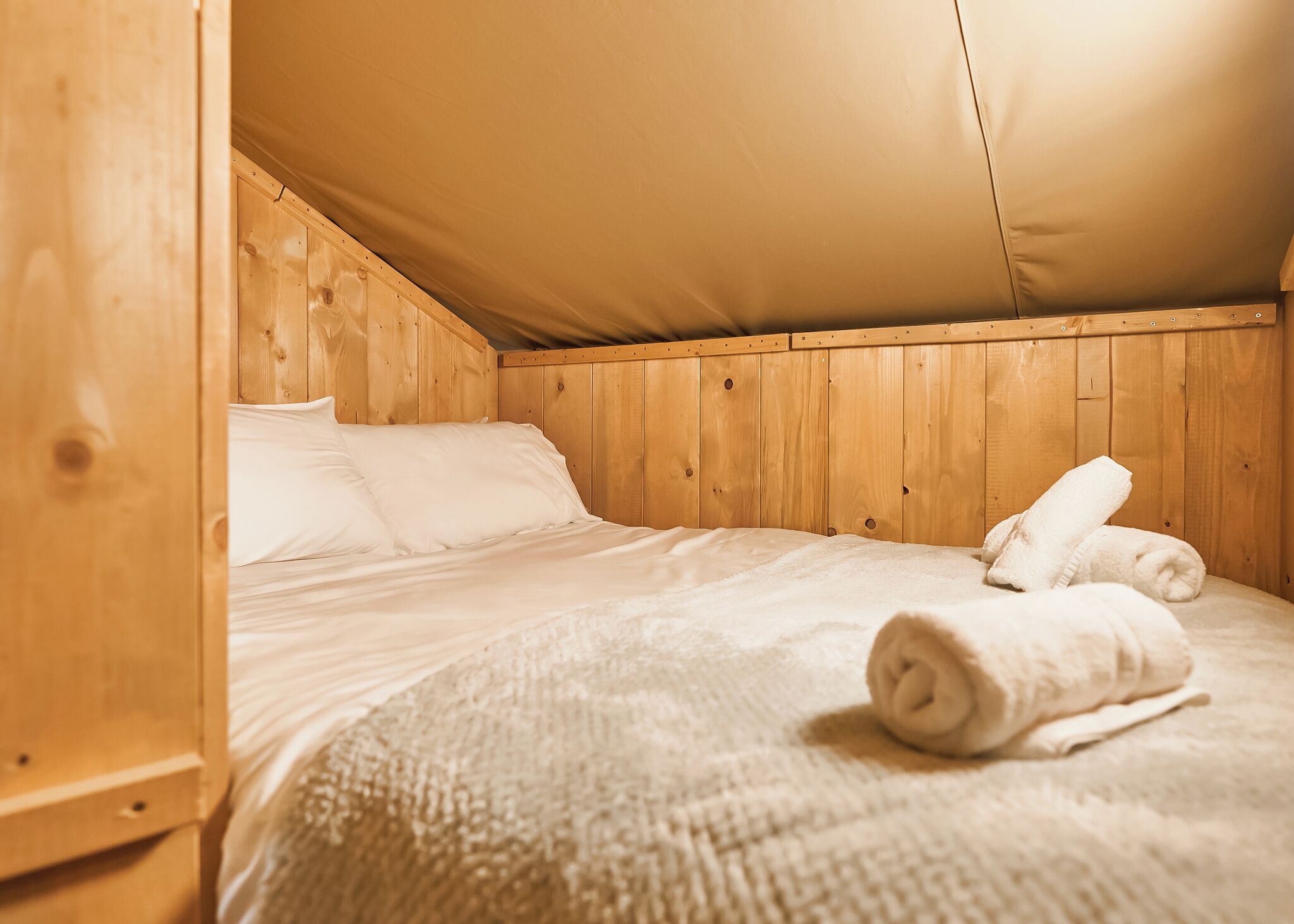 Ein Holzbett mit Etagen und weißer Bettwäsche, dazu gerollte Handtücher.