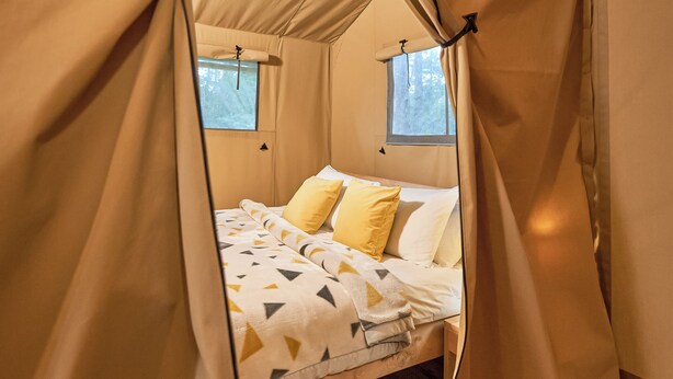 A tented room with a bed, two windows, and a view of the outdoors.