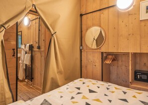 A wooden room with a bed, a round mirror, and a towel rack. - Safari Tent sleeps 6 (Hayle)