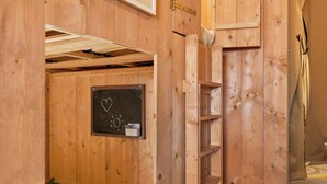 A wooden room with a chalkboard wall, a small shelf, and a mat on the floor.