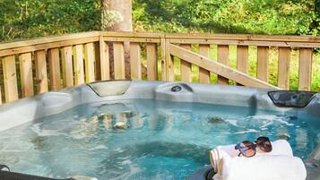 A hot tub with a wooden deck, surrounded by greenery.