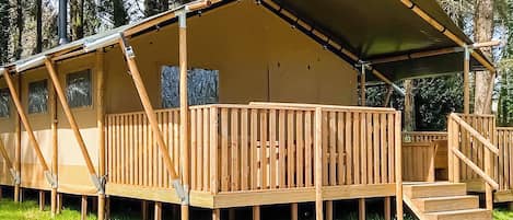 A wooden cabin with a covered deck, a staircase, and a view of the surrounding forest.