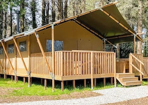 A wooden cabin with a covered deck, a staircase, and a view of the surrounding forest. - Safari Tent sleeps 6 (Hayle)