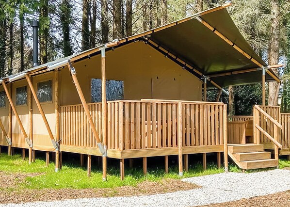 A wooden cabin with a covered deck, a staircase, and a view of the surrounding forest.
