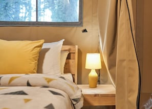 A bed with a patterned blanket, a bedside lamp, and a window with curtains. - Safari Tent sleeps 6 (Hayle)