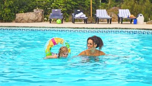A swimming pool with clear blue water, lounge chairs, and umbrellas in the background.
