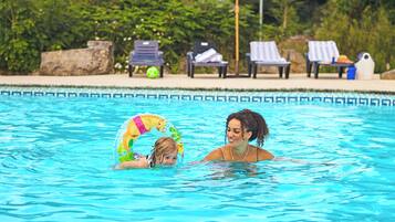 A swimming pool with clear blue water, lounge chairs, and umbrellas in the background.