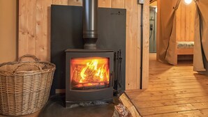 A wood-burning stove with a fire, a wicker basket, and a wooden floor.