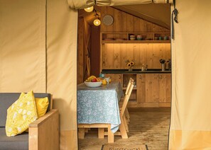 Un hébergement sous tente comprenant un espace repas, des armoires en bois et une horloge murale.