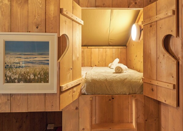 A wooden cabin-style room with a bed, a framed picture on the wall, and a small window.