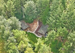 An aerial view of a cabin surrounded by dense forest, with a clear path leading to the entrance.