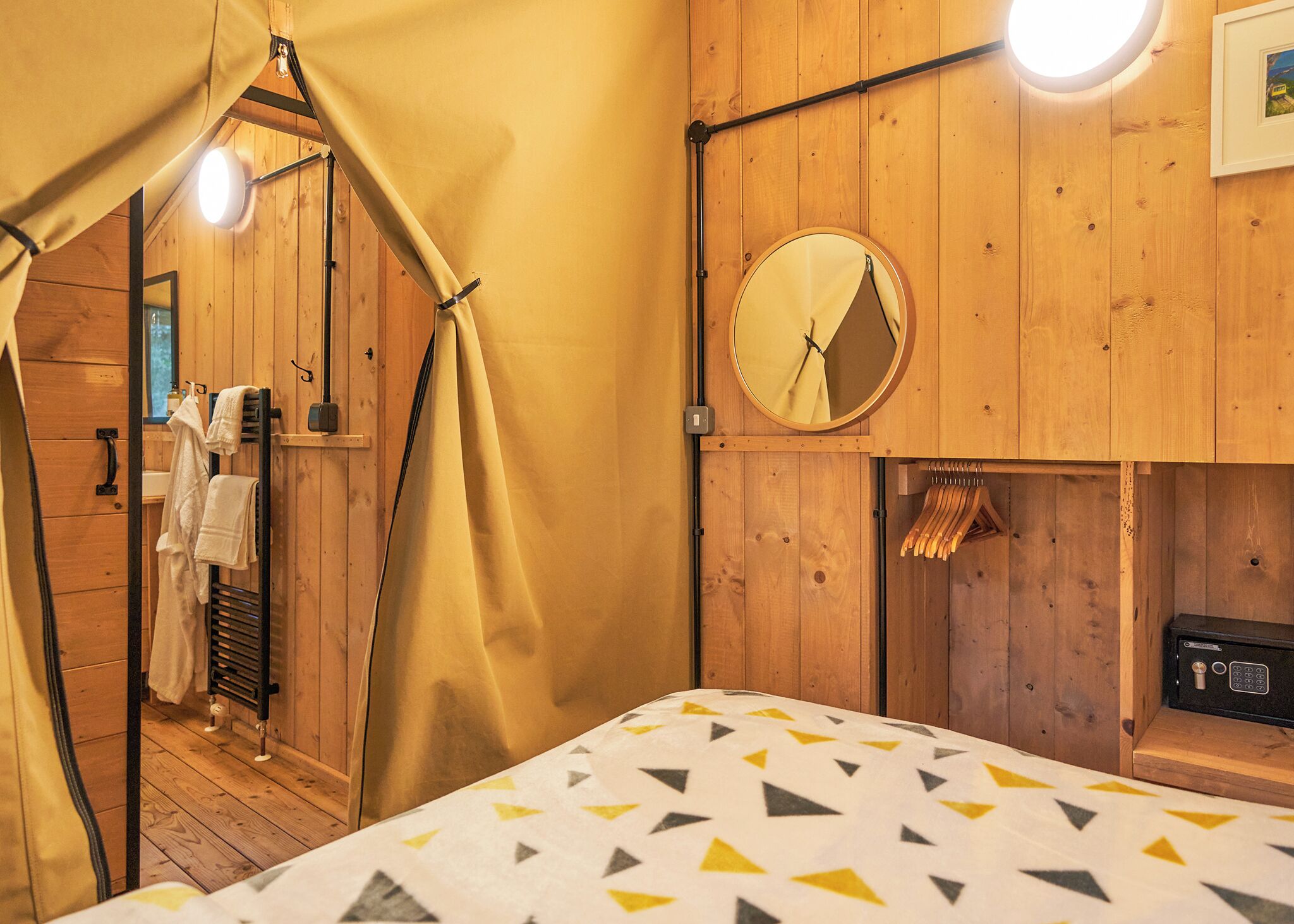 Ein Zimmer mit Holzboden, einem Bett, einem Spiegel und einem Hängegestell mit Handtüchern.