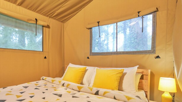 A bed with a geometric-patterned bedspread, two windows with curtains, and a bedside lamp. - Safari Tent sleeps 6 Pet Friendly (Hayle)