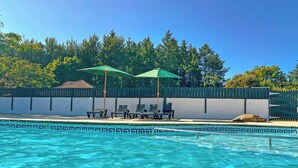 Une piscine à l’eau d’un bleu limpide, entourée d’une clôture et ombragée par deux parasols.
