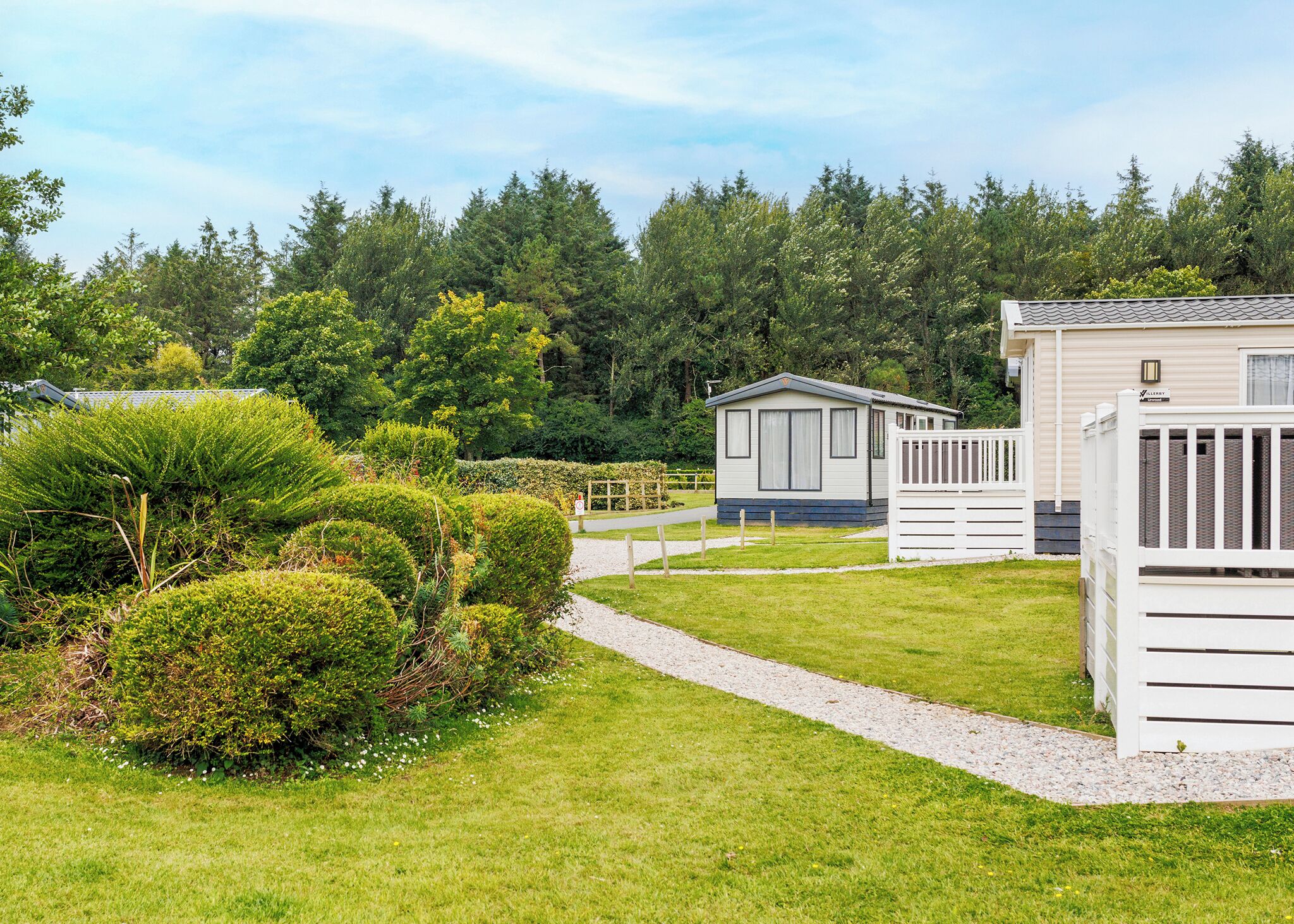 Ein Caravanpark mit ordentlich geschnittenen Hecken, einem Kiesweg und Mobilheimen.