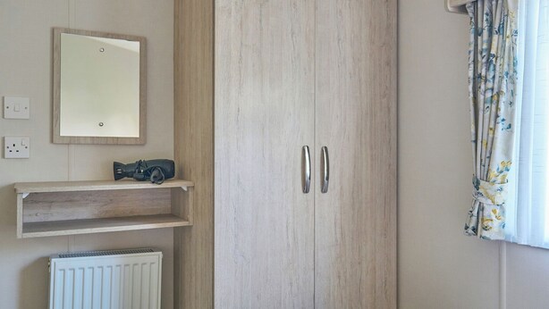 Une chambre à coucher comprenant un lit, une armoire, un radiateur, une étagère avec un appareil photo, et une fenêtre avec des rideaux.