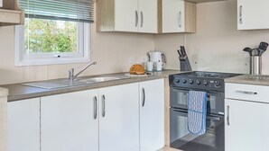 Une cuisine moderne avec des meubles blancs, un évier en acier inoxydable, une cuisinière et une fenêtre avec des stores.