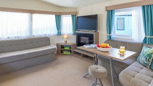 A cozy living area with a sofa, a small table with a bowl of fruit and drinks, a TV, and a fireplace. - Standard 2 Bedroom sleeps 6 Pet Friendly (Hayle)