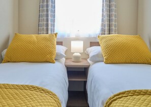 Ein Hotelzimmer mit zwei Betten, jeweils mit einem gelben gesteppten Kissen und weißer Bettwäsche. Dazwischen steht ein Nachttisch mit einer Lampe.