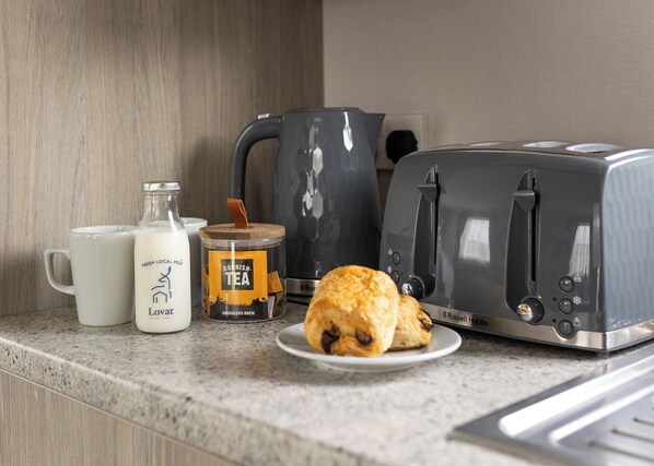 Eine Küchenarbeitsplatte mit einem Toaster, einer Tasse, einer Milchflasche, einer Teedose und einem Gebäckstück.