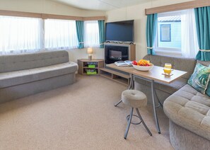 A cozy living area with a sofa, a small table with a bowl of fruit and drinks, a TV, and a fireplace. - Standard 2 Bedroom sleeps 6 Pet Friendly (Hayle)