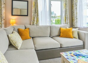 A living room with a sofa, a table with a board game, and a lamp. - The Superior 2 Bed is a comfortable and spacious sleeps 6 caravan. (Hayle)