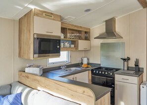 A compact kitchen with a microwave, stove, sink, and wooden cabinets. - Superior 2 Bedroom sleeps 6 (Hayle)