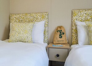A hotel room with two beds, each with a polka dot headboard and white bedding. There is a small wooden nightstand with a drawstring bag labeled 'The Big 5' by Lovet Parks. - Superior 2 Bedroom sleeps 6 (Hayle)