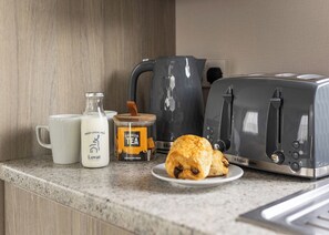 Un piano di lavoro in cucina con un tostapane, una tazza, una bottiglia di latte, un barattolo di tè e un piatto con una pasticceria.