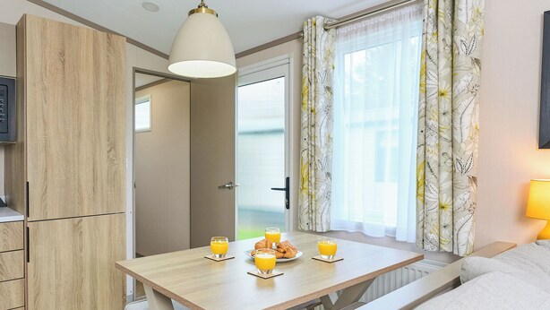 Une chambre moderne avec une table en bois mise pour le petit-déjeuner, un lit, une armoire et une fenêtre avec des rideaux.