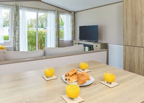 A modern room with a sofa by a window, a flat-screen TV, a dining table with croissants and orange juice, and a radiator.