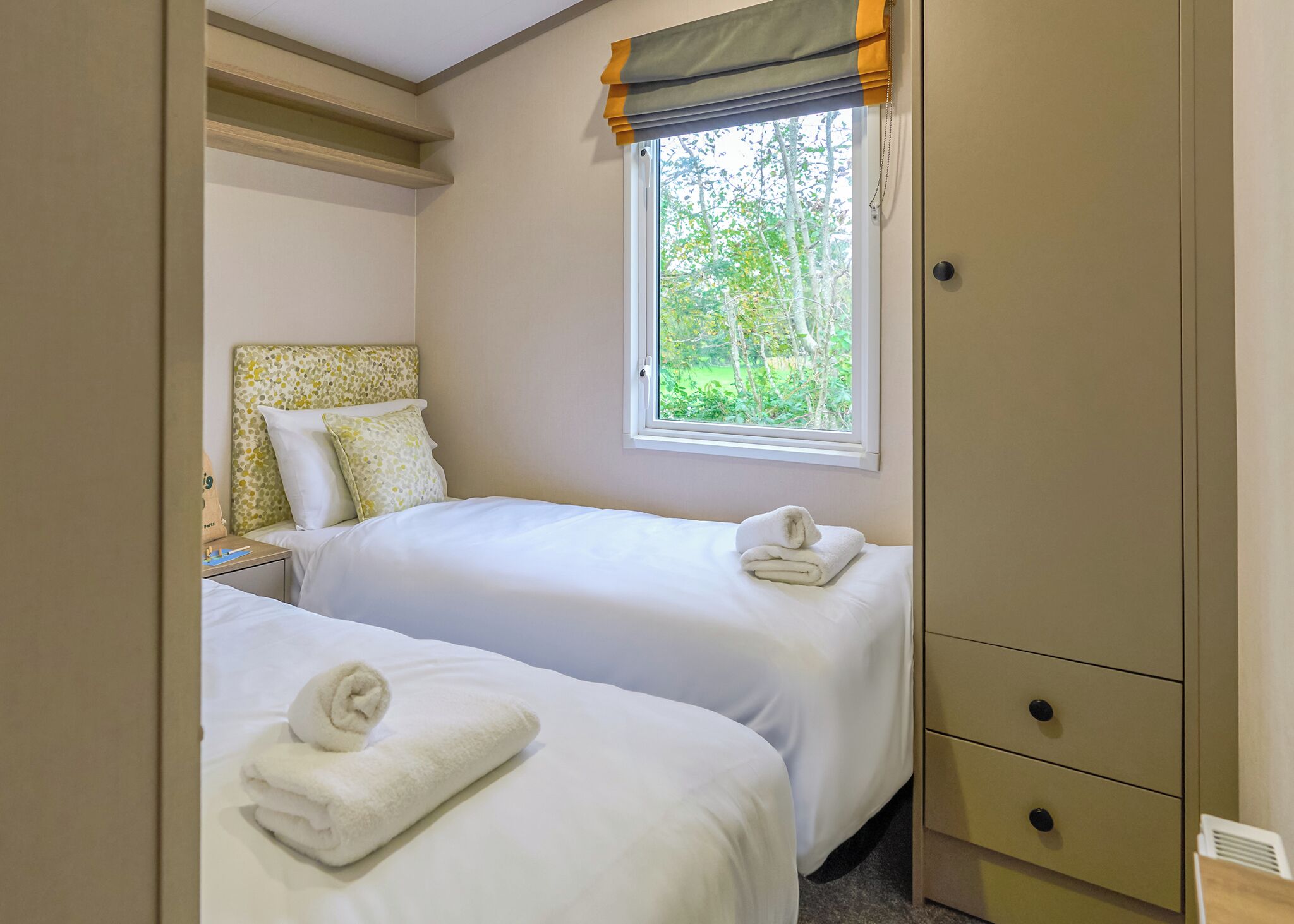 A bedroom with two beds, a window with a view of trees, and a wardrobe.