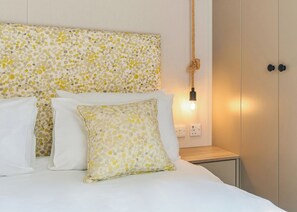 A bed with white bedding and patterned pillows, a bedside table with a lamp, and a wall-mounted light fixture. - Superior 2 Bedroom sleeps 6 Pet Friendly (Hayle)