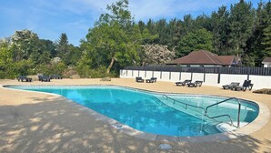 Une piscine entourée d’arbres et d’une clôture, avec des chaises longues à proximité.
